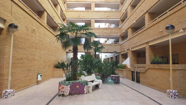 A multi-level atrium with a central seating area, surrounded by brick walls and potted plants. - ACV - Costa Azahar I-2ª linea planta 3 norte (OROPESA)