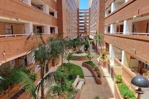 Un edificio de varios pisos con un patio central que tiene palmeras, bancos y jardineras.