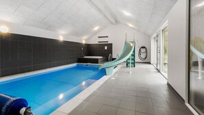 A modern indoor swimming pool with a slide, a jacuzzi, and a sauna.