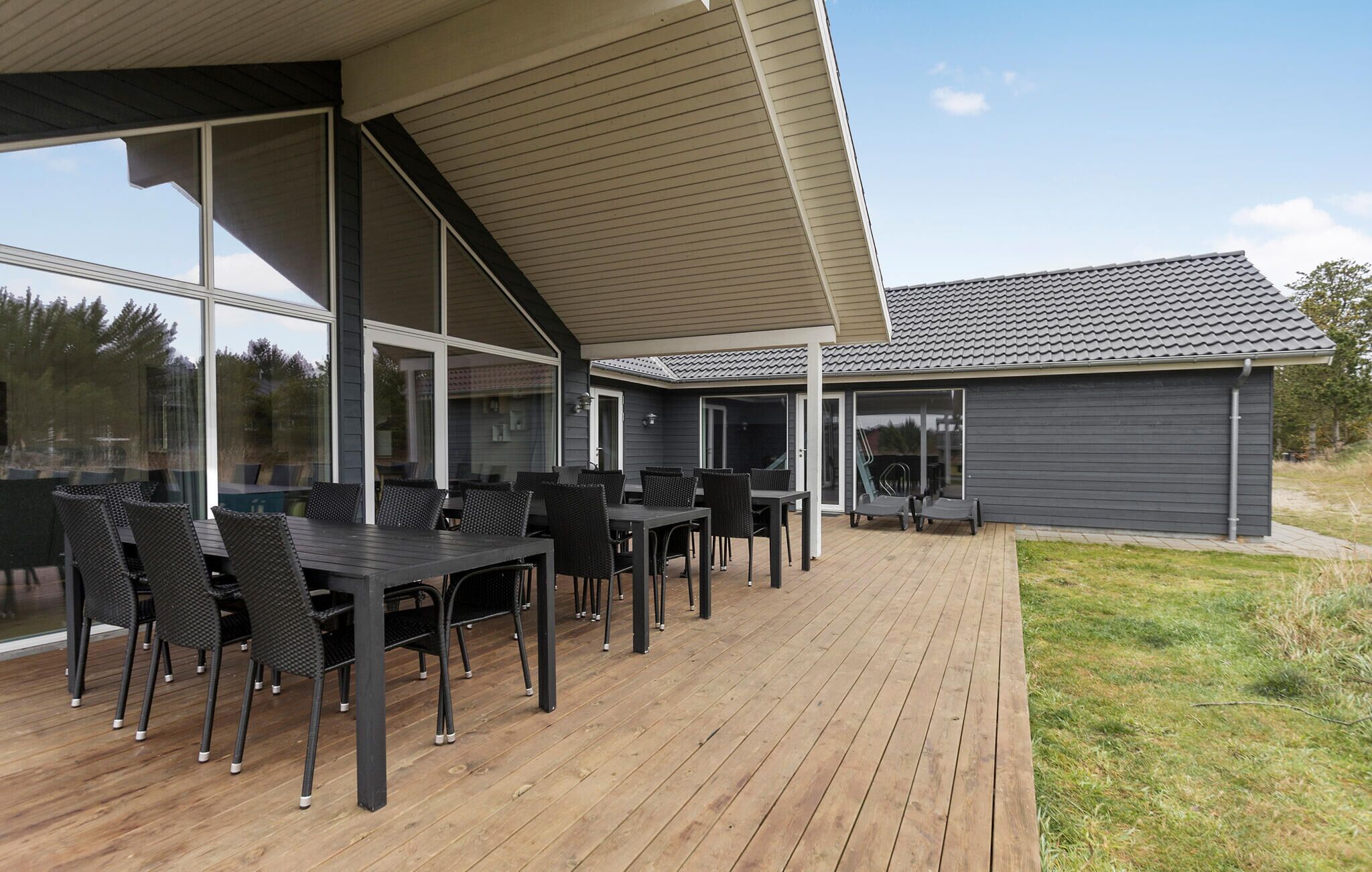 Una veranda esterna coperta con pavimento in legno e mobili in rattan nero.