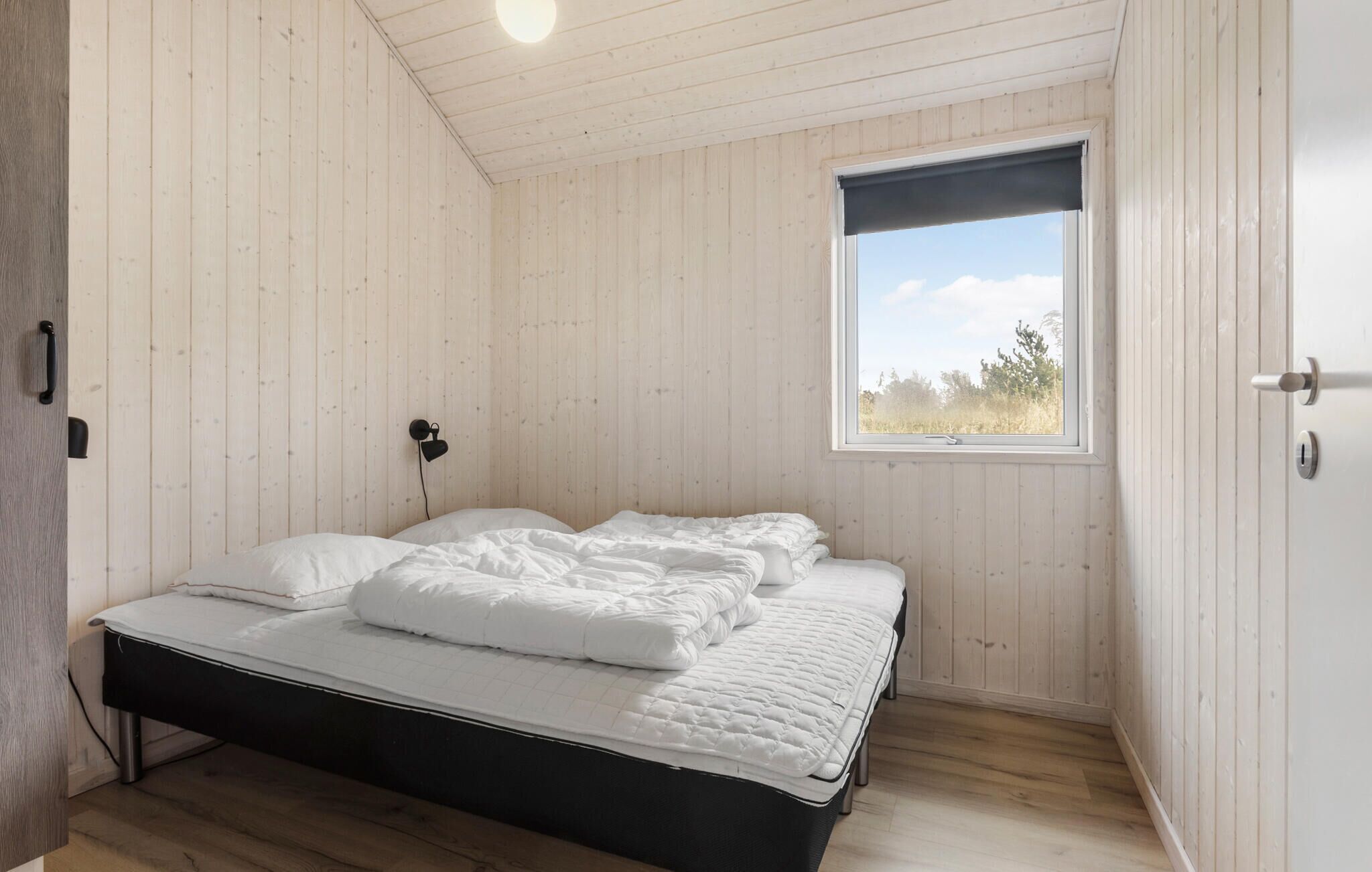 Un dormitorio con cama, paredes de madera, una ventana y una puerta.