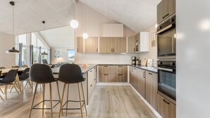 A modern kitchen with wooden cabinets, a large island with stools, stainless steel appliances, and pendant lighting.
