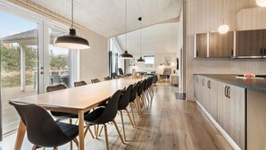 A modern kitchen with wooden cabinets, a long dining table, and pendant lighting.