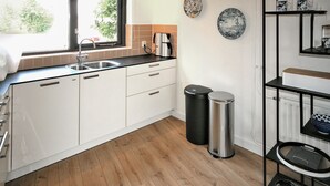 A modern kitchen with white cabinets, a stainless steel sink, a coffee maker, a trash bin, and a shelf with decorative items. - 2 bedroom beautiful home in Lemmer (Lemmer)