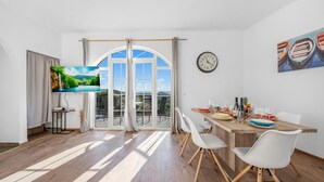 Uma zona de refeições moderna com uma mesa de madeira, cadeiras brancas e vista para uma paisagem montanhosa através de grandes janelas.