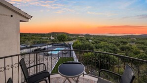 Uma varanda com piscina, cadeiras e vista para o campo ao pôr do sol.