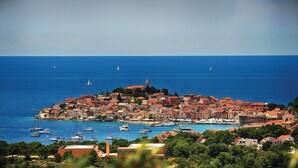 Uma vila costeira com um conjunto denso de edifícios, uma igreja imponente e uma vista clara do mar com vários veleiros.
