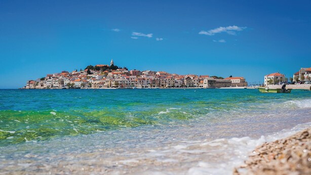 Uma cidade costeira com edifícios ao longo da orla, águas azuis cristalinas e um barco na praia.