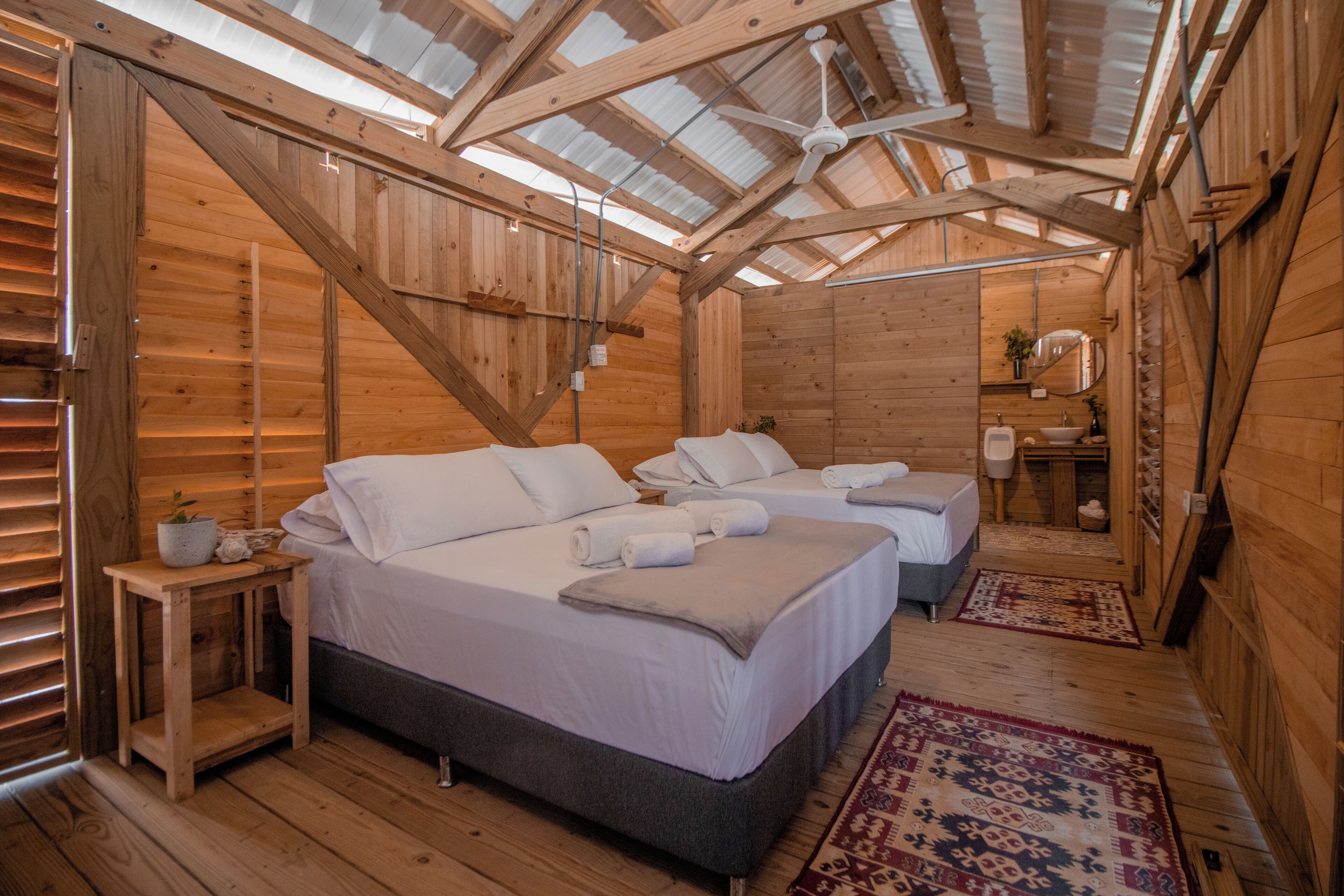 A wooden cabin with two beds, a ceiling fan, and a skylight.