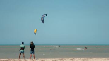 A beach with people flying kites and a person surfing.