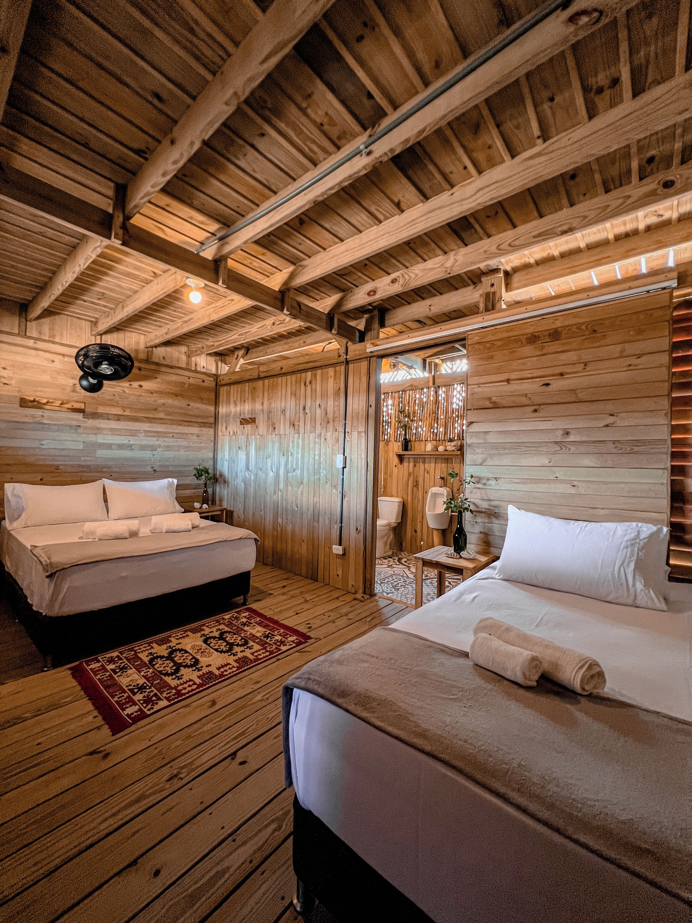 Una cabaña de madera con dos camas, piso de madera y techo con vigas a la vista.