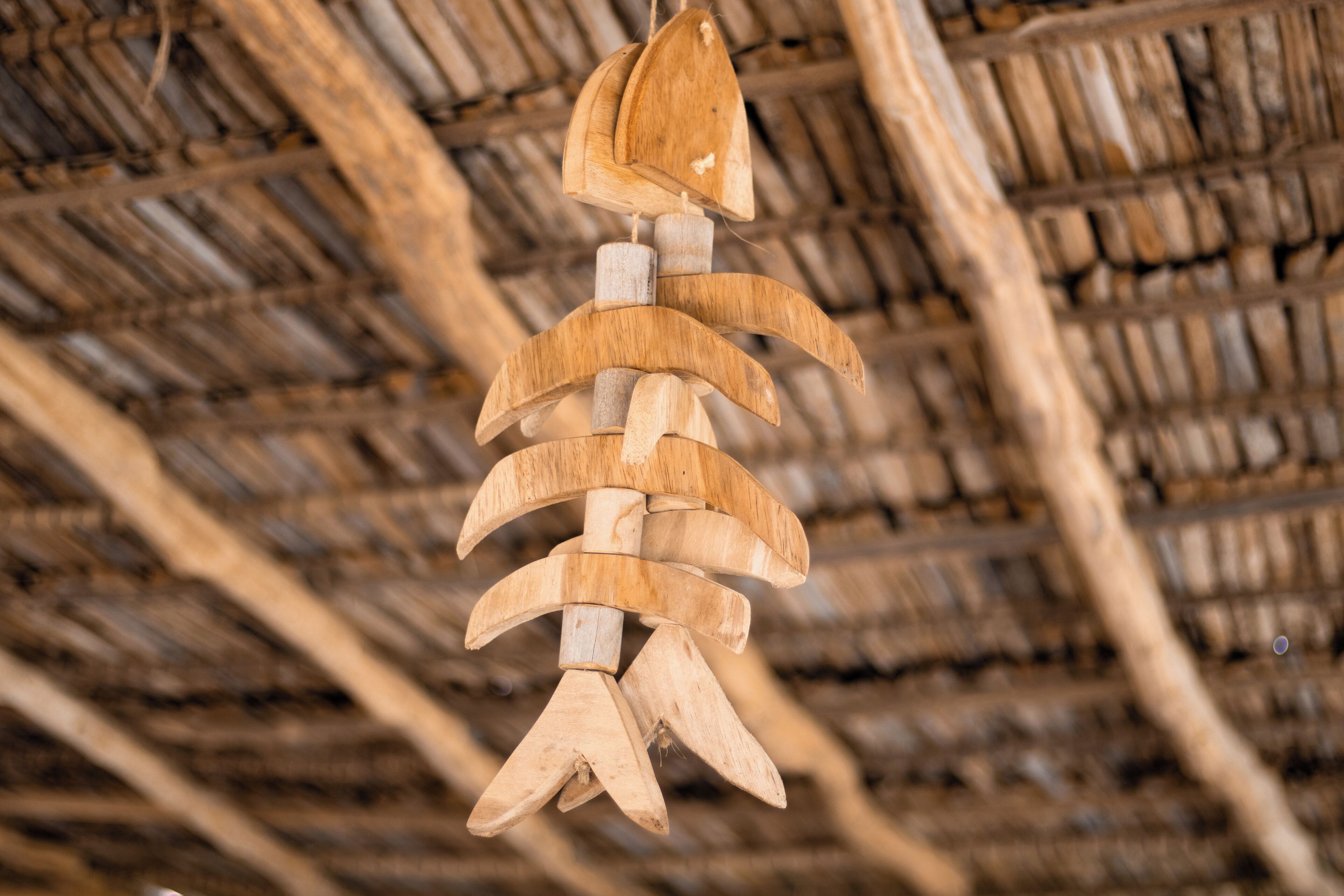 Un móvil de madera colgando de una estructura de techo de paja.