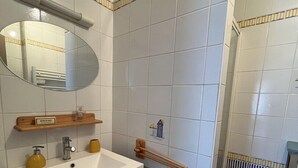 Ein Badezimmer mit weißem Waschbecken, Spiegel und Handtuchhalter. Eine Lüftungsanlage ist an der Wand zu sehen.