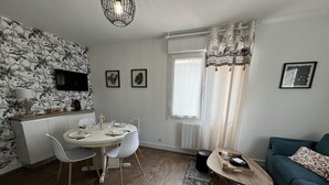 Ein modernes Wohnzimmer mit Essbereich, einer Couch, einem Fernseher und einem Fenster mit Vorhängen.