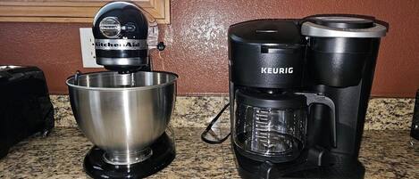 A kitchen with a mixer, a coffee maker, and a bowl on a granite countertop.