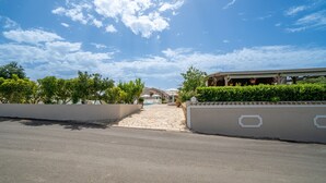 A paved driveway leading to a building with a covered entrance, surrounded by greenery and a clear sky. - Apartment 'Premier Studio Downstairs 9' with Sea View, Wi-Fi and Air Conditioning (arillas kerkyra)