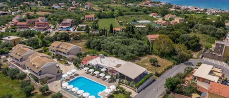 An aerial view of a coastal residential area with a swimming pool, houses, and a road.