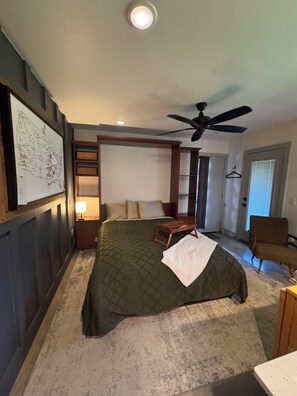A bedroom with a bed, a ceiling fan, a map on the wall, and a door leading to another room.