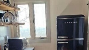 Eine Küche mit einem schwarzen Kühlschrank, einem Fenster und einer Mülltonne.