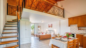 Um quarto espaçoso com escada, cama, mesa de jantar com cadeiras e área de cozinha.