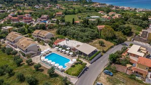Vista aérea de uma área residencial à beira-mar, com piscina, casas e estrada.