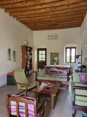 Een ruime woonkamer met een hoog houten plafond, een centrale tafel en meerdere zithoeken.