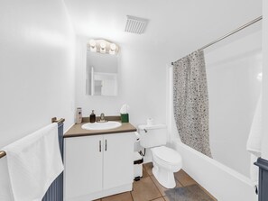 A bathroom with a white sink, mirror, and toilet. There is a towel rack with a white towel, a shower curtain, and a small green soap dish. - Access to the beach and riverside trail. (Windsor)