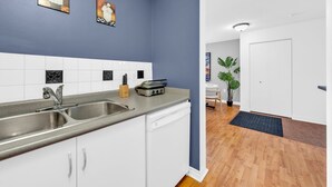 Une cuisine moderne avec des meubles blancs, un évier en acier inoxydable et un grille-pain. Deux tableaux encadrés sont accrochés au mur.