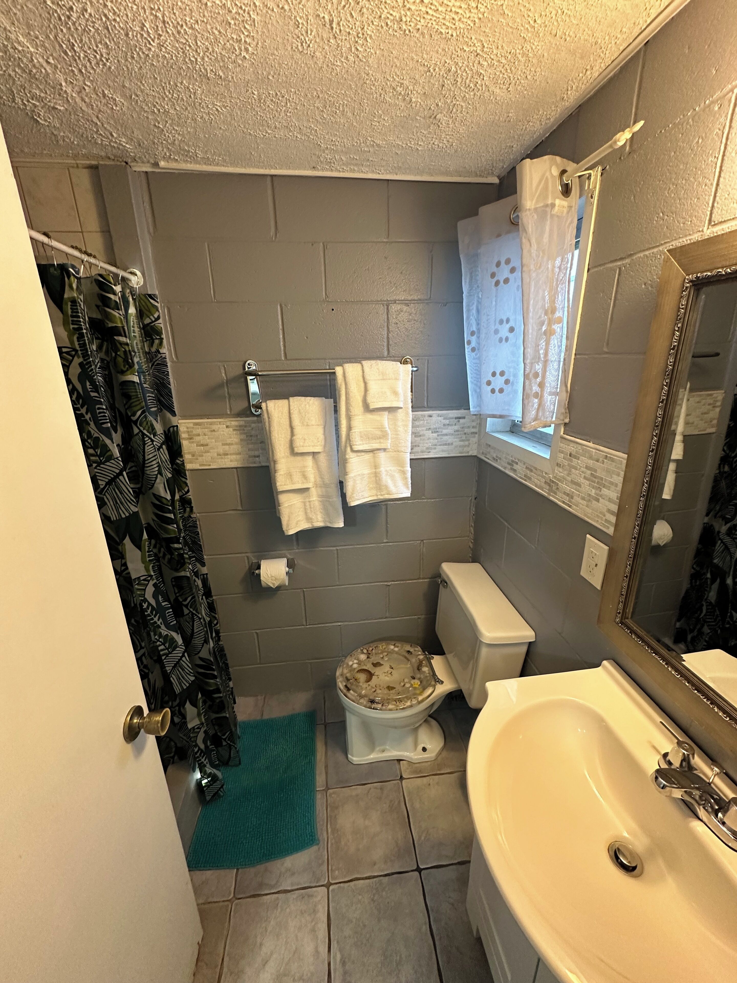 A small bathroom with a toilet, sink, and a mirror. There are towels hanging on the wall and a shower curtain.