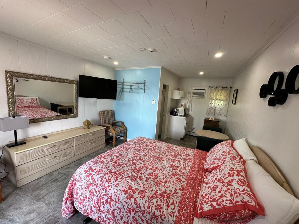 A bedroom with a bed, dresser, mirror, TV, and a small desk.