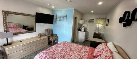 A bedroom with a bed, dresser, mirror, TV, and a small desk.