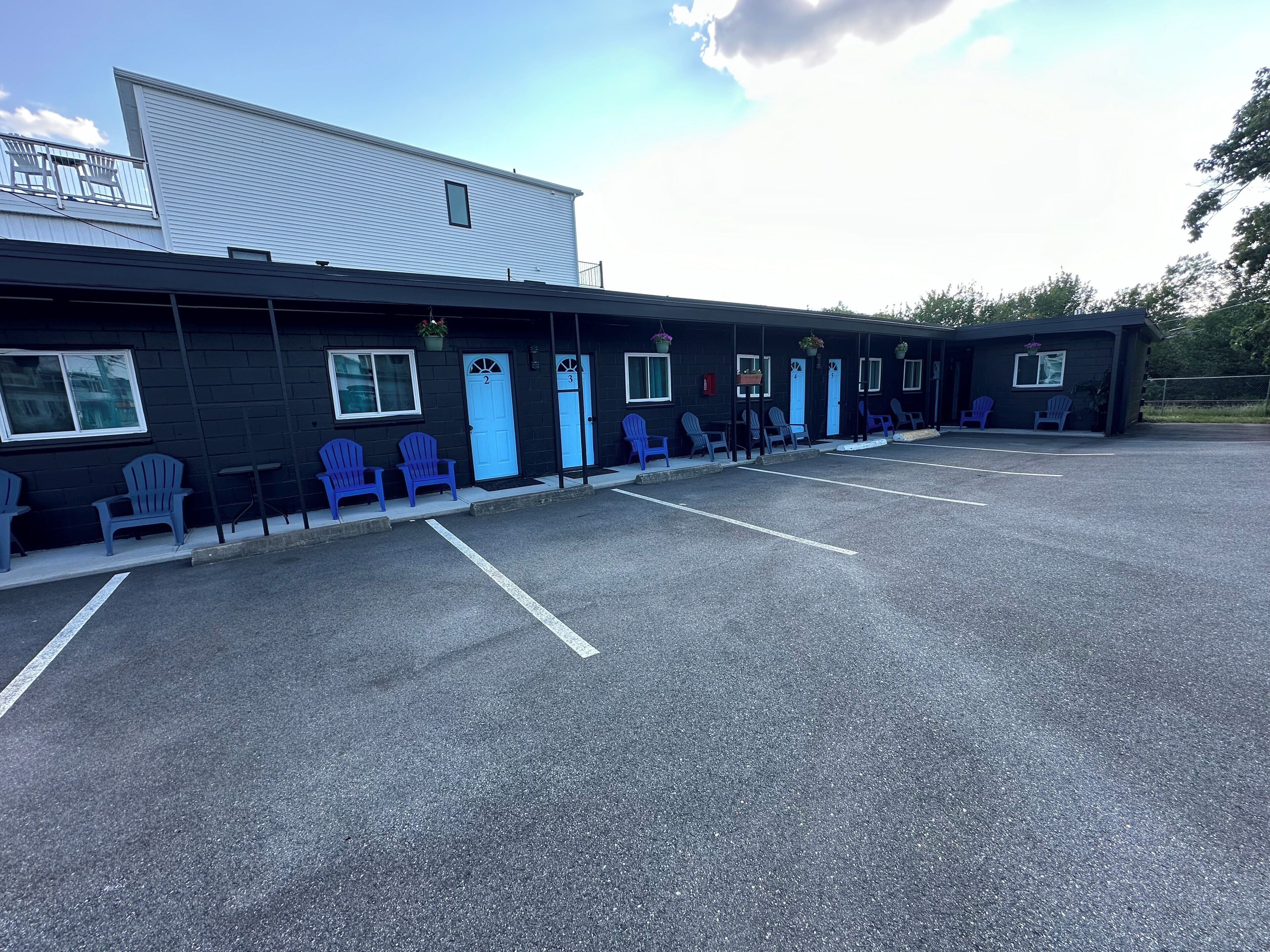 A motel with numbered doors, blue chairs outside, and a parking lot.