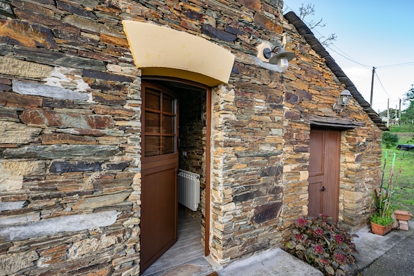 Ein Steinhaus mit Holztür und kleinem Garten mit Topfpflanzen.