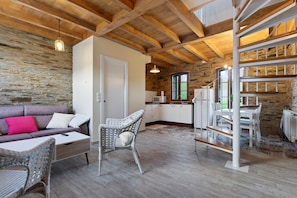 Ein rustikaler Innenraum mit freiliegenden Holzbalken, Steinwänden, einer Couch, Korbmöbeln und einer Treppe.