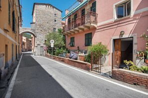 Una calle estrecha con edificios de piedra, una señal de límite de velocidad de 20 km/h y una entrada con reja a un edificio rosa.