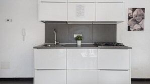 Moderni keittiö, jossa on valkoiset kaapit, ruostumattomasta teräksestä valmistettu liesituuletin, pieni ruukkukasvi ja kaasuliesi.