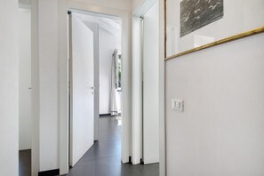 A hallway with white walls, a door leading to another room, and a framed picture on the wall.