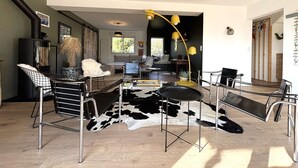 Ett modernt vardagsrum med en svartvit matta av kohud, stolar med metallram, en svart soffa och en gul golvlampa.