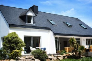 Ein modernes Haus mit Satteldach, Dachfenstern und einem gepflegten Garten mit Steinen und Sträuchern.