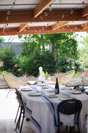 Ein Essbereich im Freien mit einer Holz-Pergola, Lichterketten und einem für vier Personen gedeckten Tisch mit Stühlen.