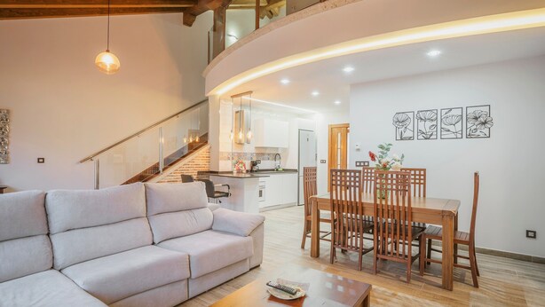 Una sala moderna con sofá, mesa de comedor, sillas, una escalera y una cocina.