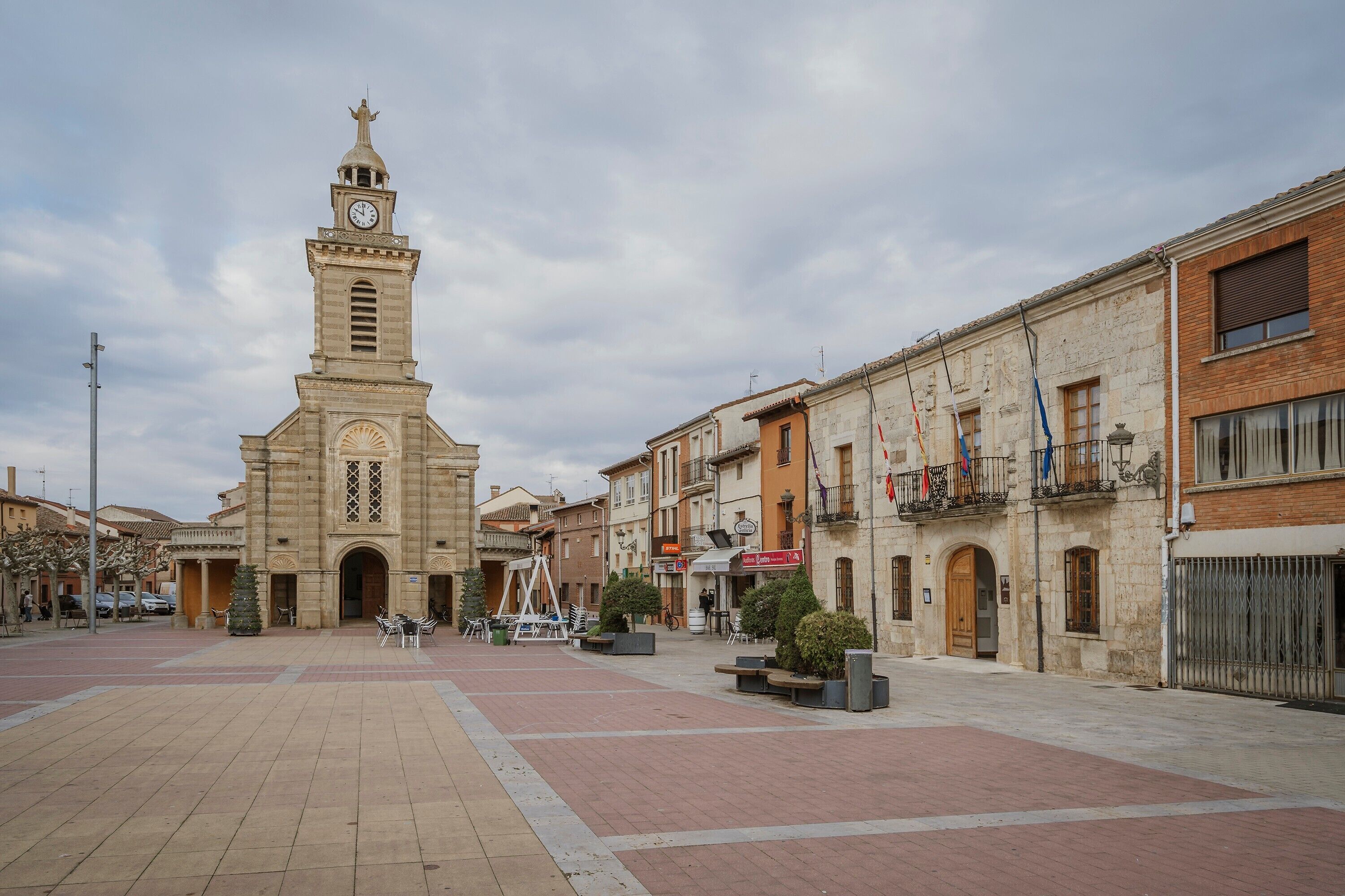 A square with a historic building featuring a clock tower, paved walkways, and outdoor seating areas.