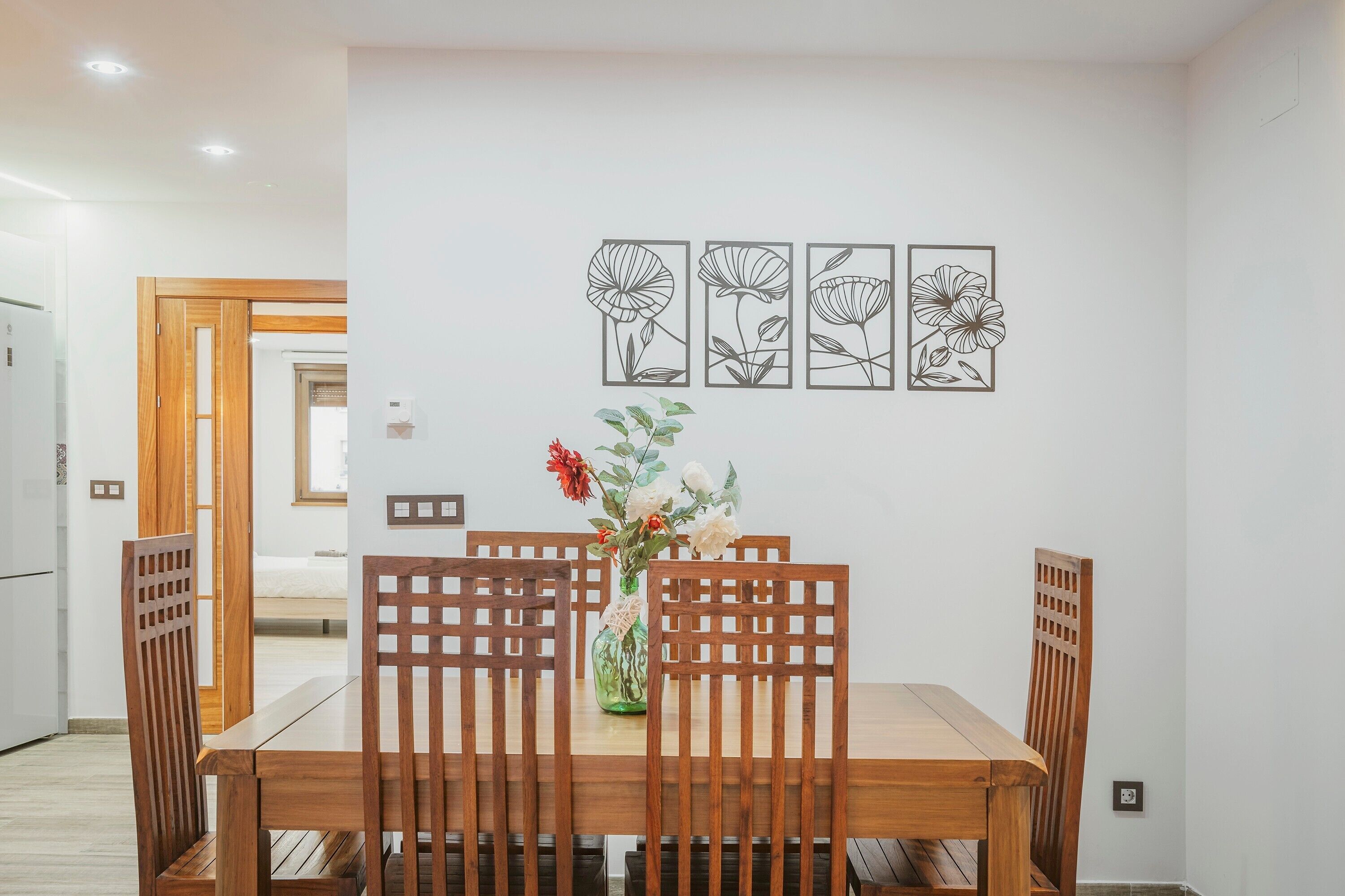 A dining area with a wooden table and chairs, a vase with flowers, and three framed floral artworks on the wall.