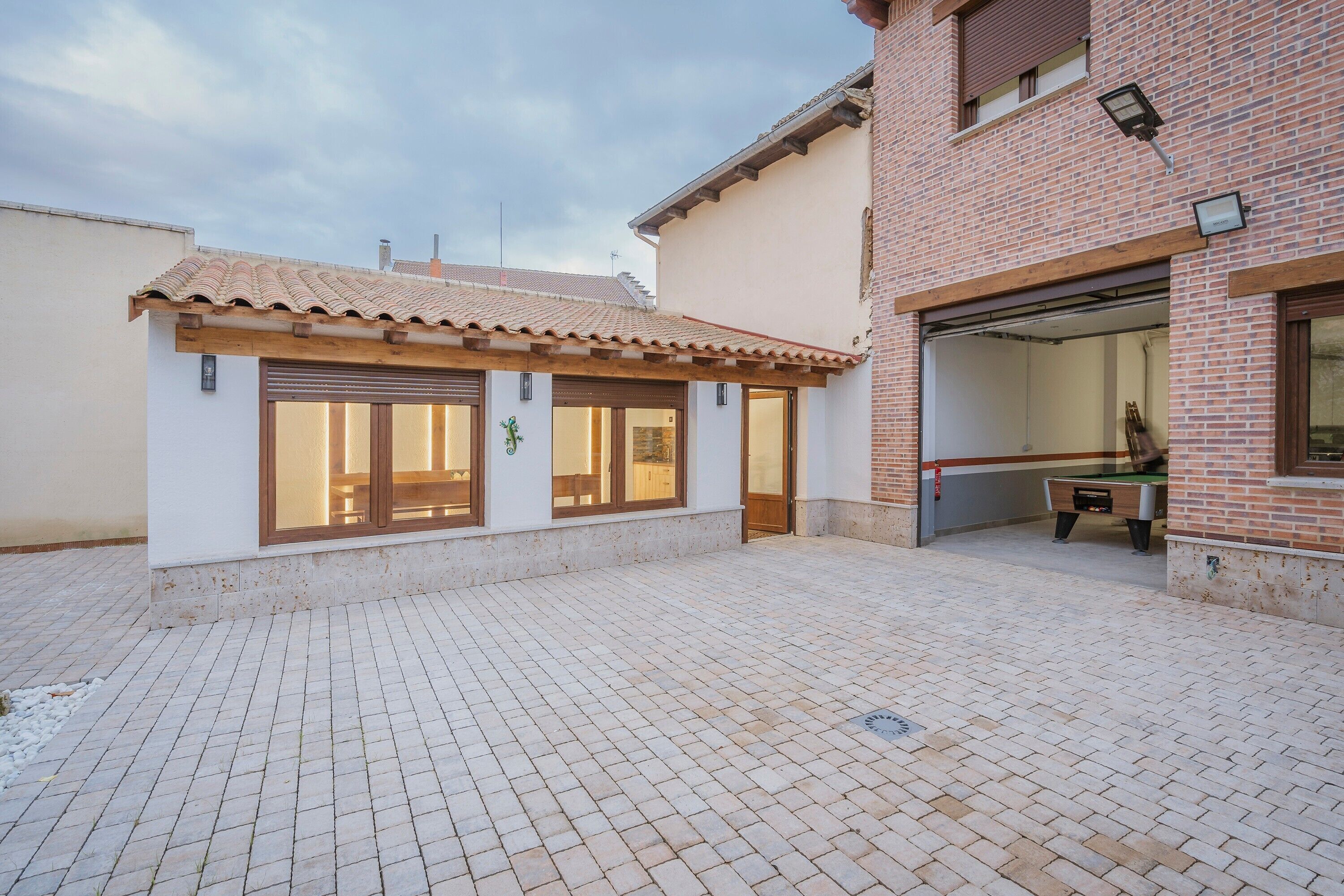 A courtyard with a tiled floor, a small building with large windows, and a garage door.