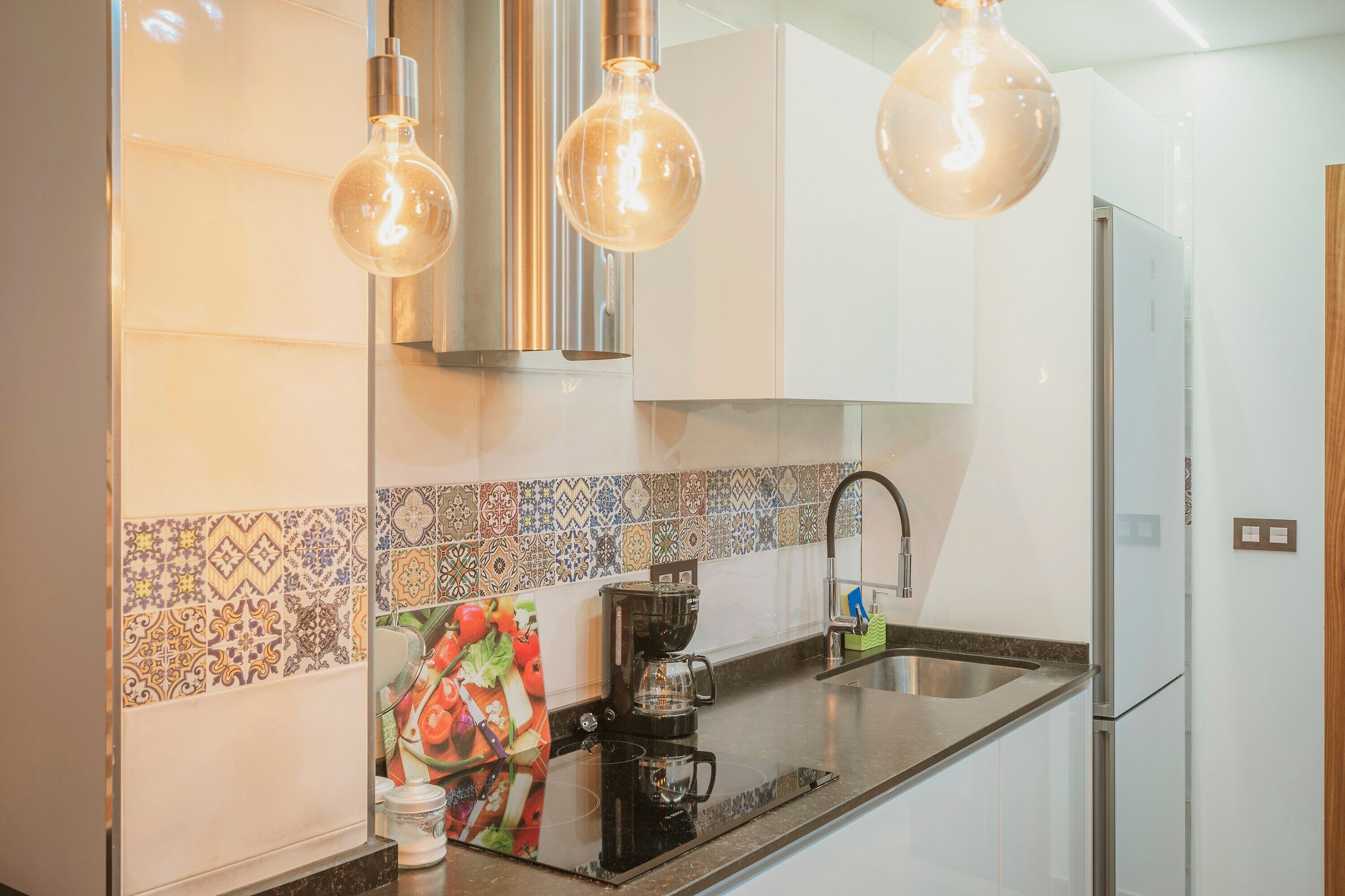 A modern kitchen with a coffee maker, stainless steel appliances, and decorative tiles.