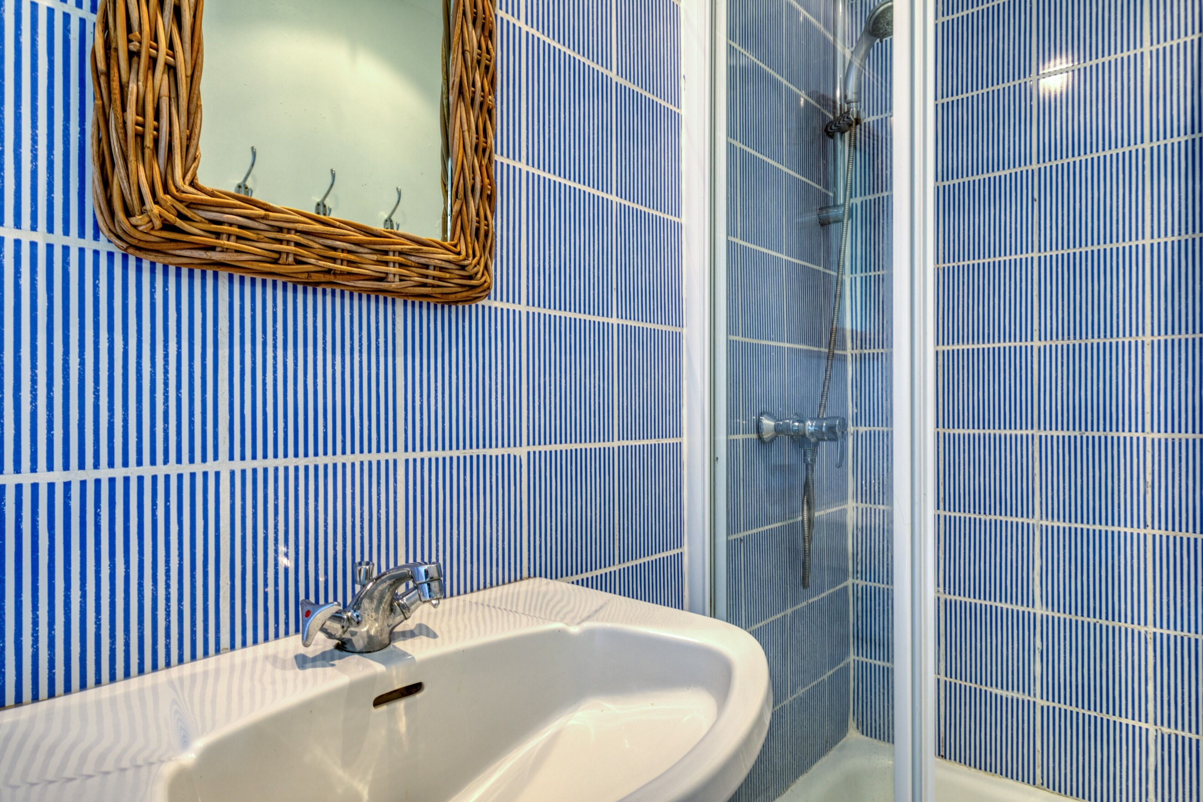 A bathroom with a white sink, a mirror with a wicker frame, and blue striped tiles.