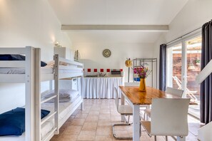 A bunk bed room with a kitchen area, a dining table with chairs, and a view of the outside.