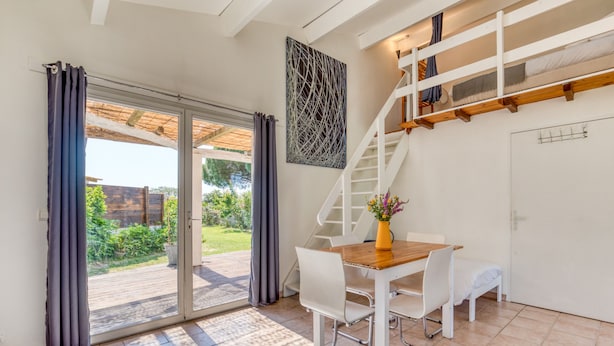 Een modern interieur met een houten eettafel, witte stoelen, een trap en een glazen schuifdeur die leidt naar een buitenruimte.