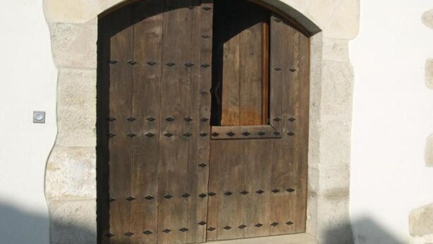 Une porte en bois, ornée de clous métalliques, encadrée par un arc en pierre.