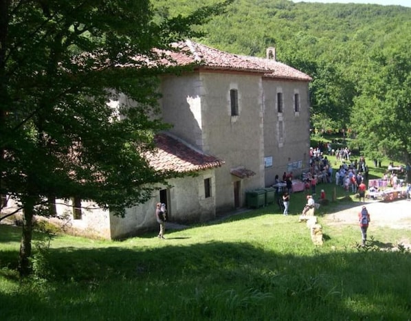 A rustic building with a tiled roof, surrounded by lush greenery and a crowd of people.